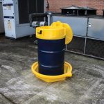 Yellow drum tray under a blue 210L drum outdoors, designed to catch spills and enhance safety in industrial settings.