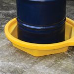 Yellow drum tray with a blue 210-liter drum, preventing spills on concrete for safe, easy industrial storage.